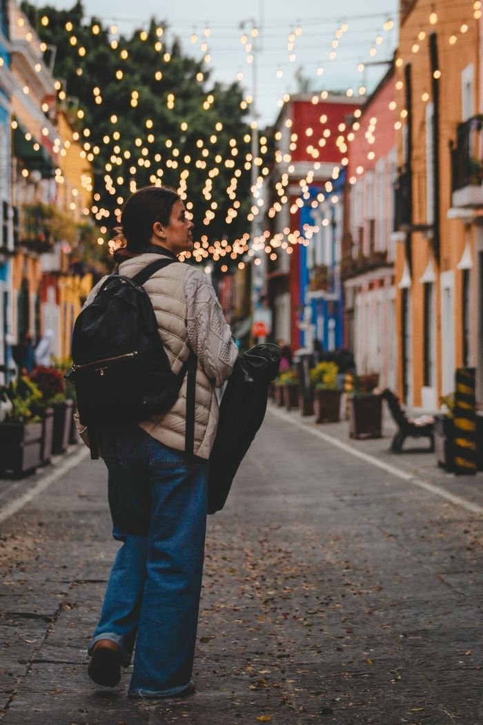 A person strolls down a vibrant street with twinkling lights overhead, capturing a festive urban vibe.