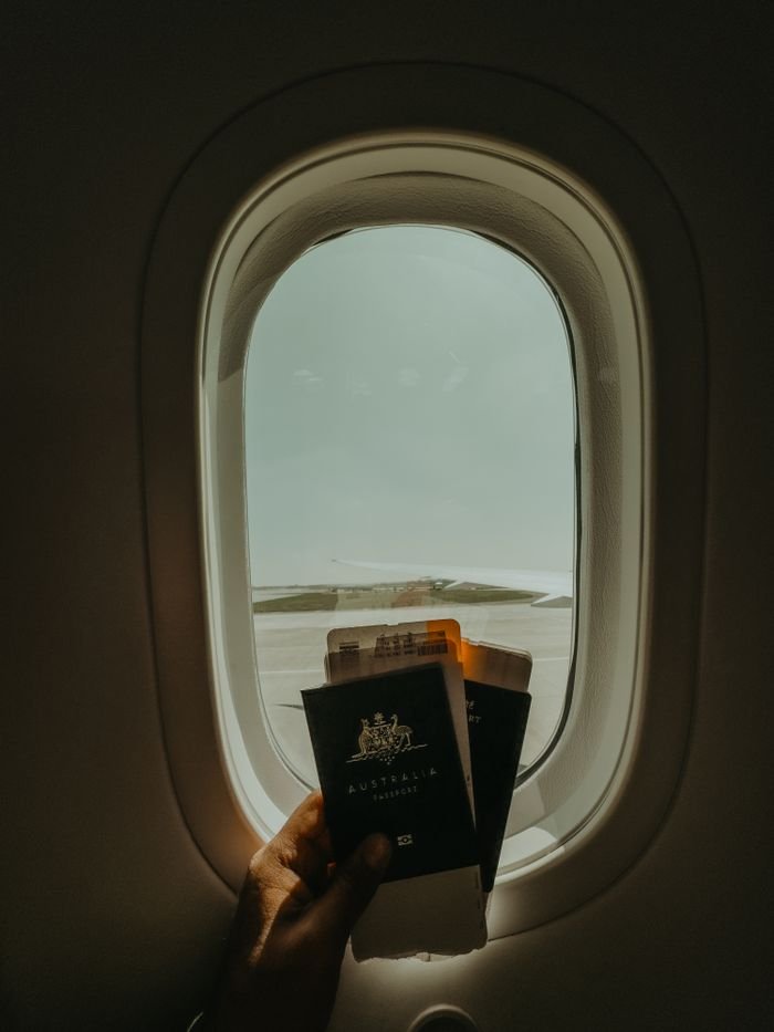 Hand holding passport and tickets by airplane window, preparing for travel adventure.